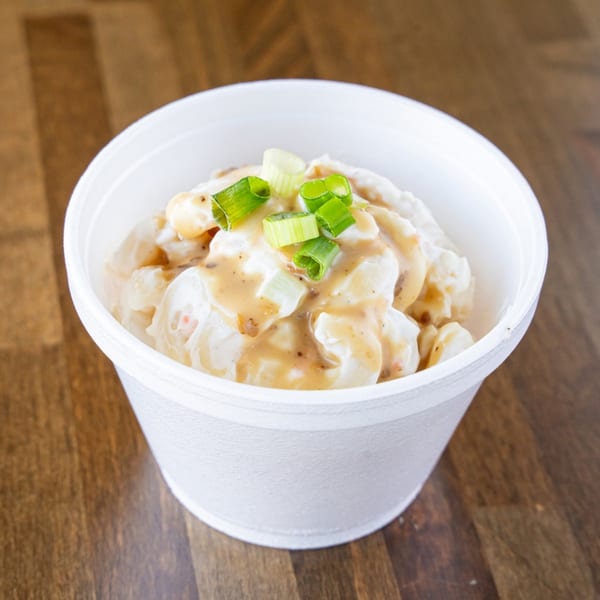 Hawaiian macaroni salad with gravy and green onions in a white styrofoam cup.