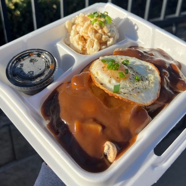 Legends Pacific Island Grill's Loco Moco with gravy, fried egg, macaroni salad, and sauce in a takeout container.