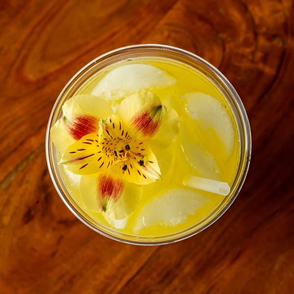 Overhead view of a vibrant yellow Hawaiian drink with ice, garnished with a yellow and red flower.